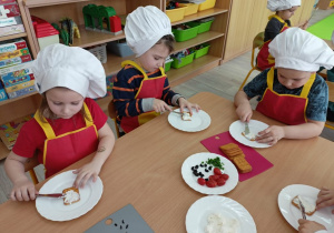 Troje dzieci skupione na smarowaniu ciasteczek serkiem.